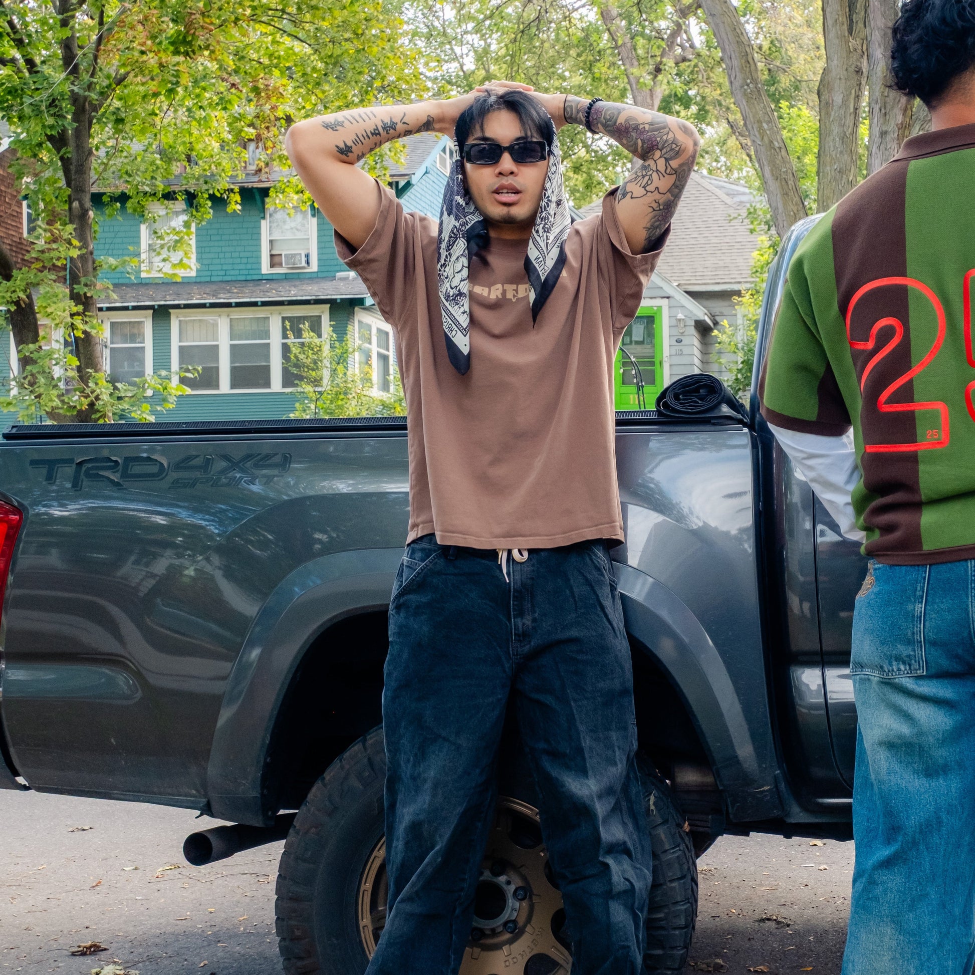 Person standing in front of a truck with another person partially visible, outdoors.