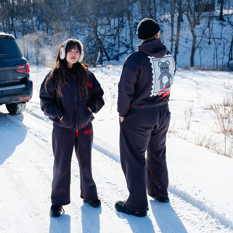 Two people standing in a snowy landscape with a vehicle in the background.